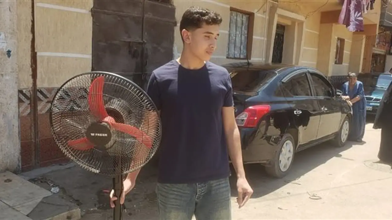شاب يحضر مروحة لشقيقته أمام لجنة امتحانات الثانوية العامة بالبحيرة لمواجهة حرارة الطقس